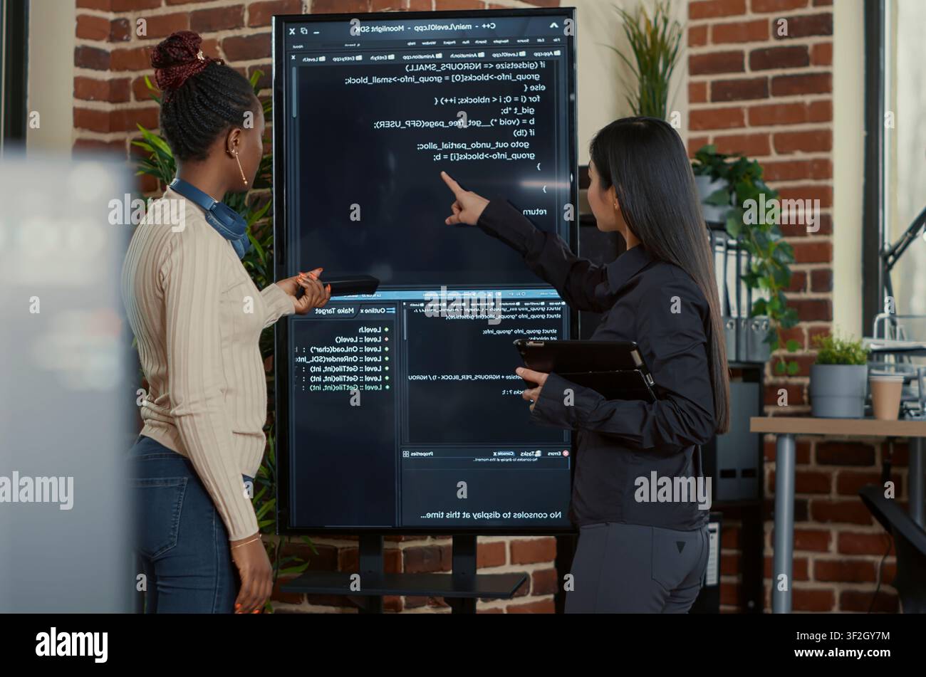 Programming team searches for code bugs as engineers use a tablet and wall display to review bugs, cloud computing and team software development in an IT office. Stock Photo