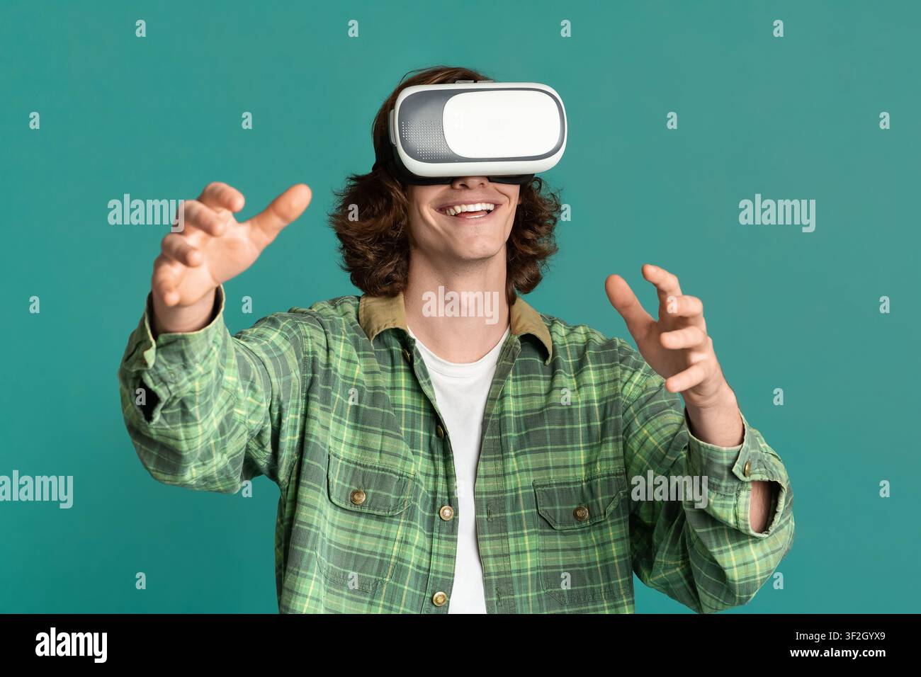 Young guy in virtual reality headset playing computer games on turquoise background Stock Photo