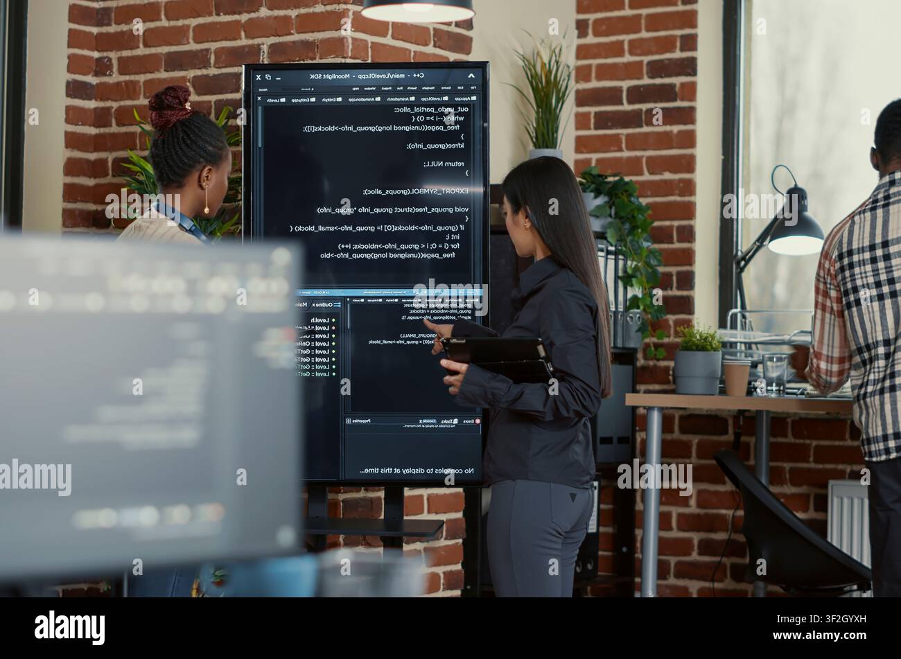 Engineer explains wall screen code errors as engineers use a tablet and wall display to review bugs, cloud computing and team software development in an IT office. Stock Photo