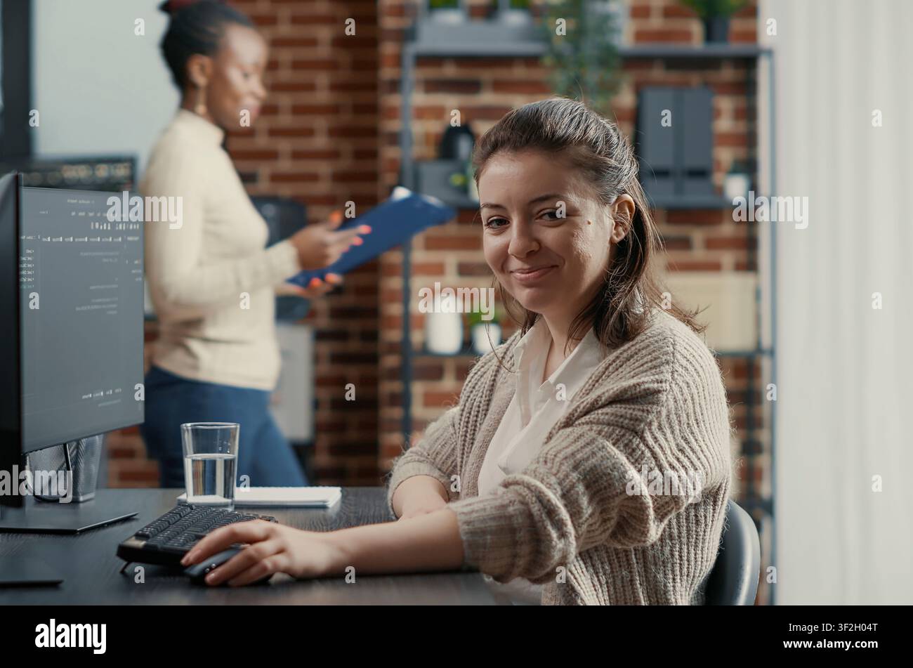 Programmer types source code on a computer keyboard, turning with a confident smile while working on software development in a technology office. Stock Photo