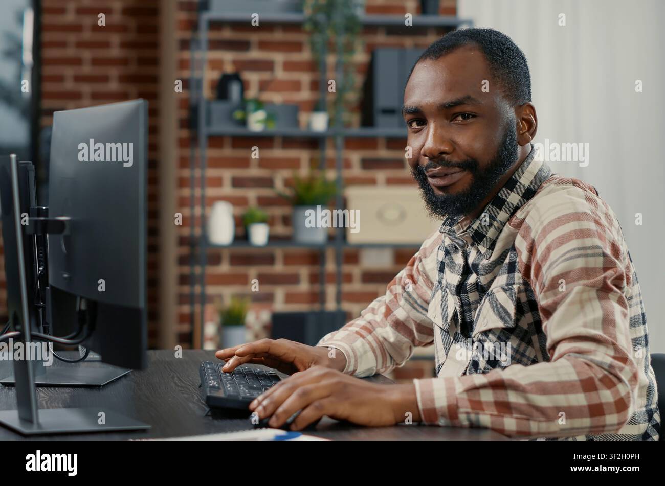 Programmer typing programming code on computer keyboard turning head and smiling while colleague walks by in background, software engineer sitting at desk writing code feeling confident. Stock Photo
