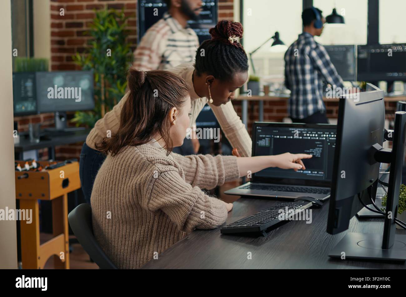 Two software coders analyzing source code looking for errors running on laptop screen while sitting at desk, team of system engineers working on cyber security innovation in busy server room. Stock Photo