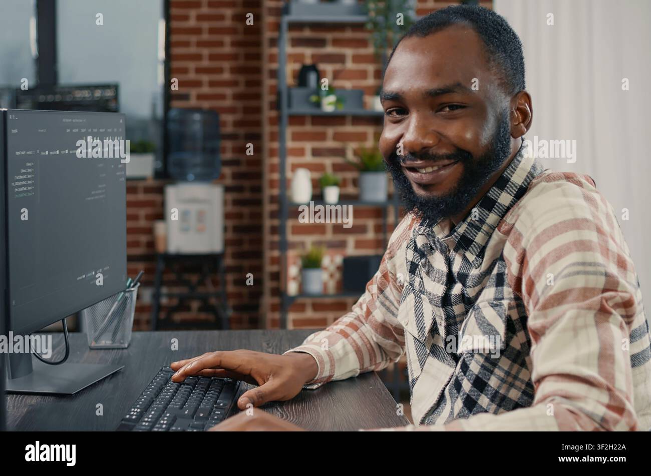 Software developer types programming code on a computer keyboard, turning with a confident smile while working on online cloud computing in an office. Stock Photo