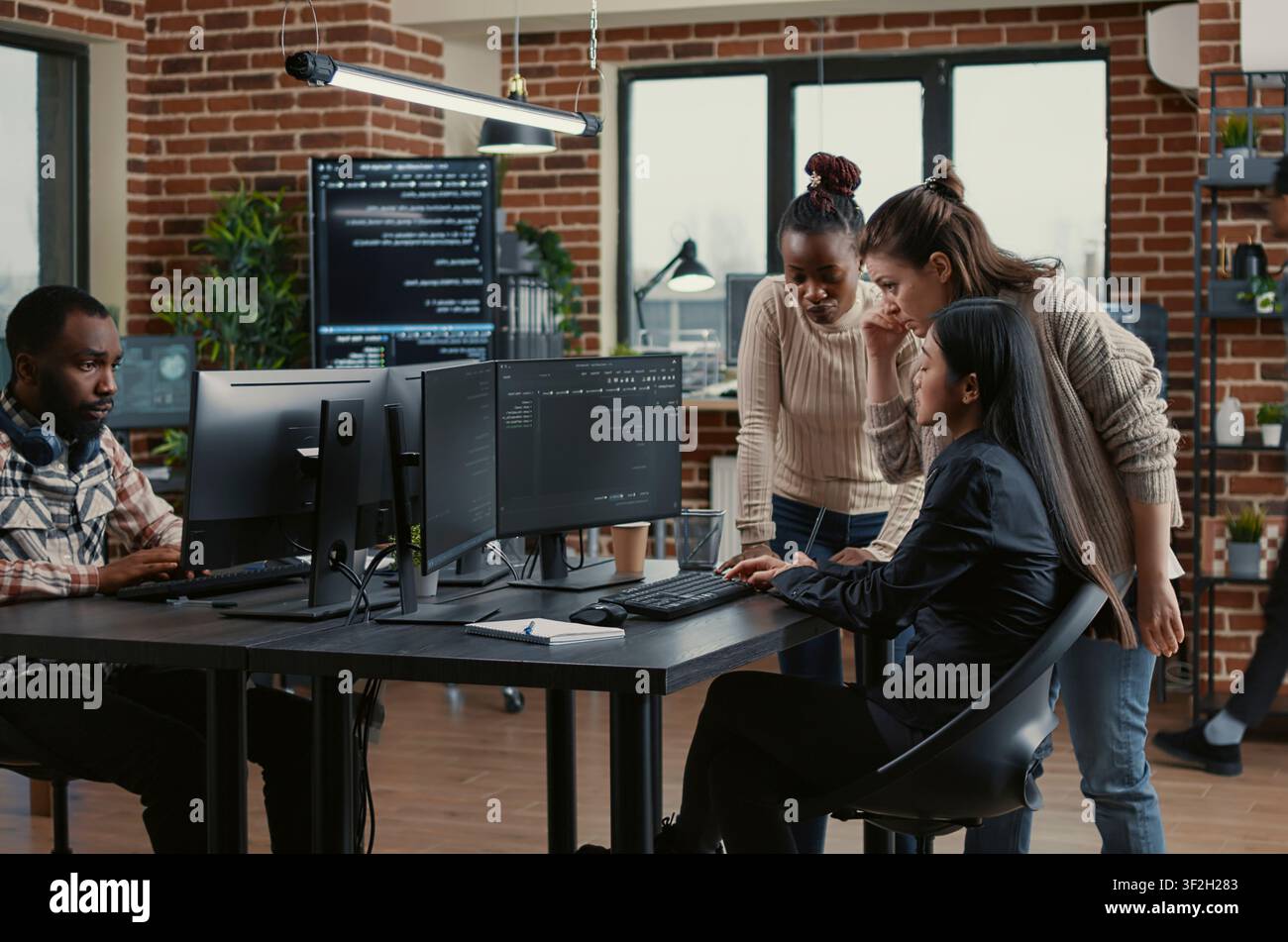 Diverse engineers brainstorm software code library while a developer team discusses algorithms, database work and new software ideas across office computer screens. Stock Photo