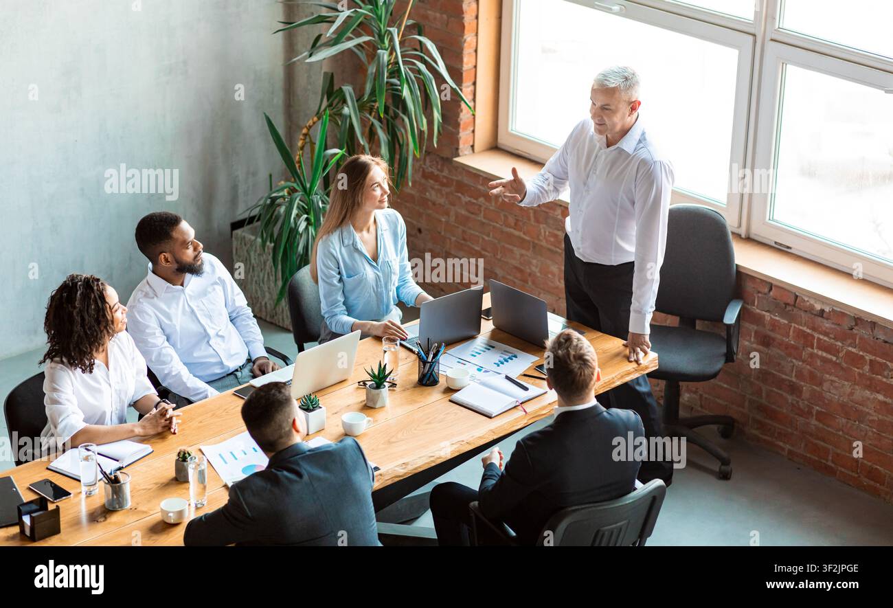 Employer Giving Speech On Meeting With Employees Sitting In Office Stock Photo
