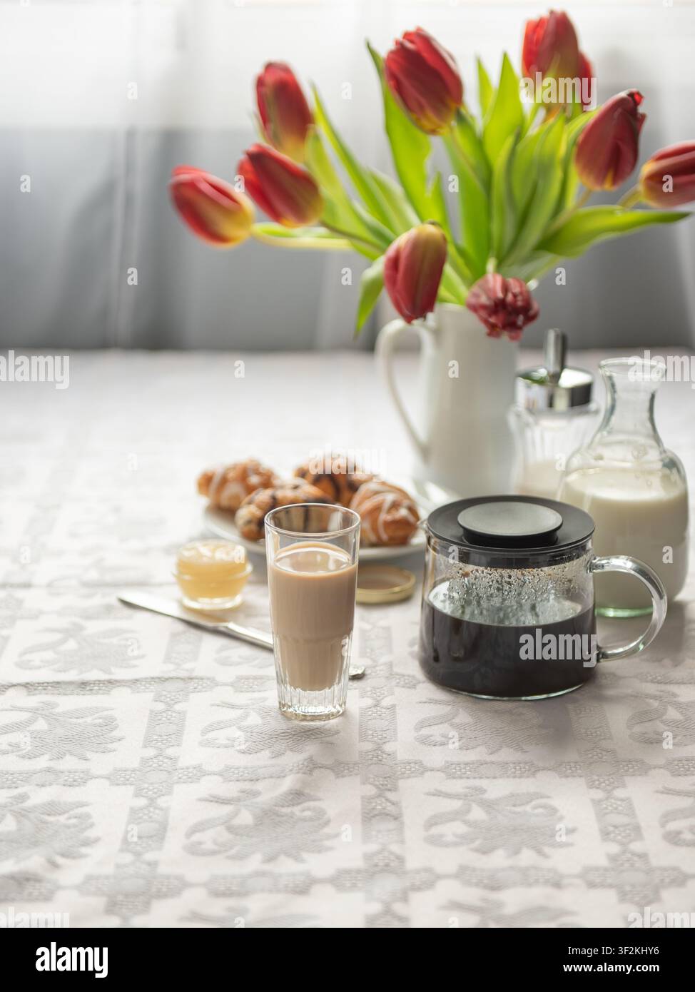 Morning coffee with milk, croissants and red tulips on table. Stock Photo