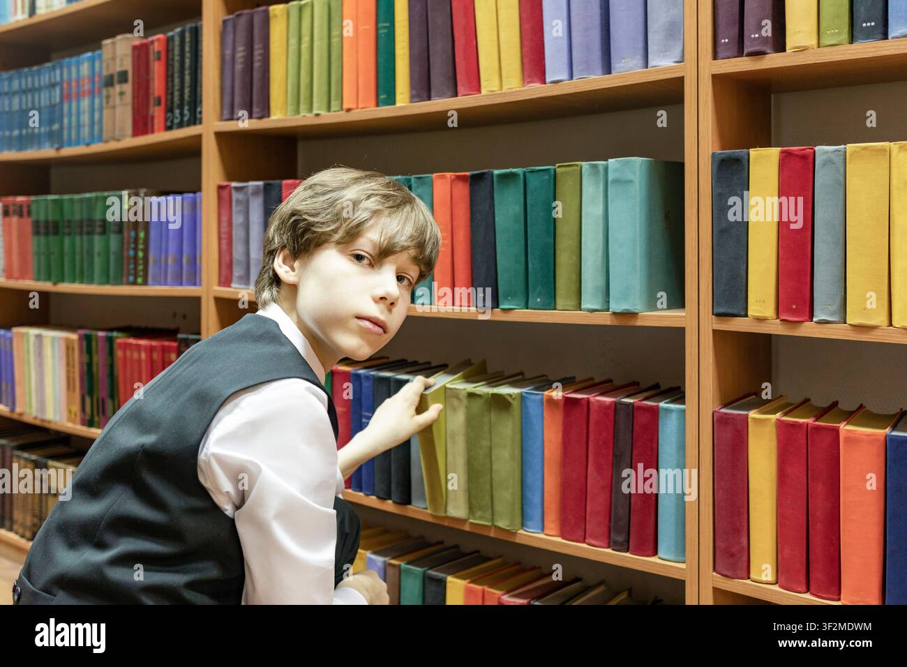 Schoolboy Choosing Book from Library Shelf Stock Photo