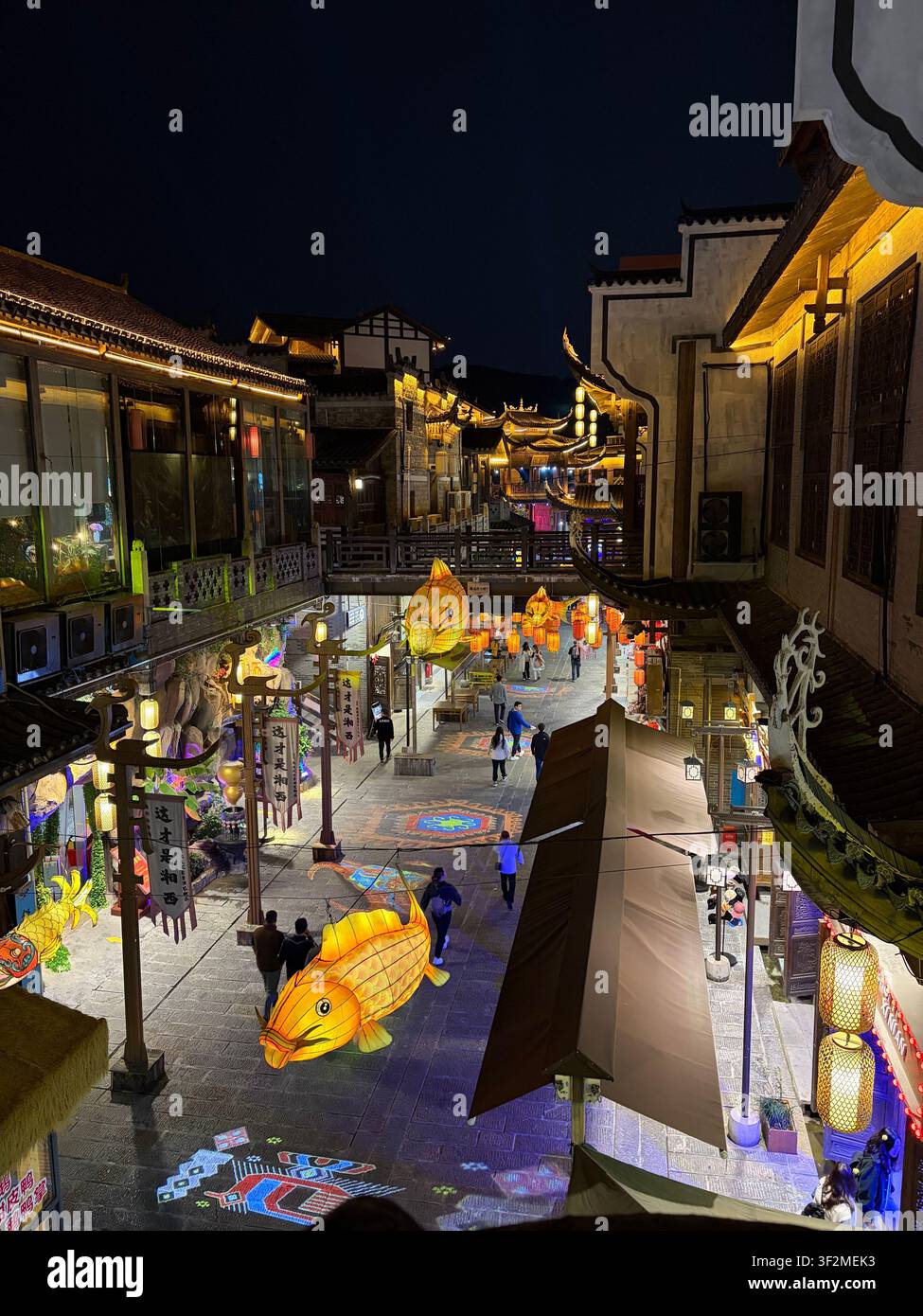 5 November 2025, Zhangjiajie, Hunan, China - Colorful fish-shaped lanterns illuminate a bustling traditional night market street with pagoda architecture and visitors. - Smartphone Captured Stock Image