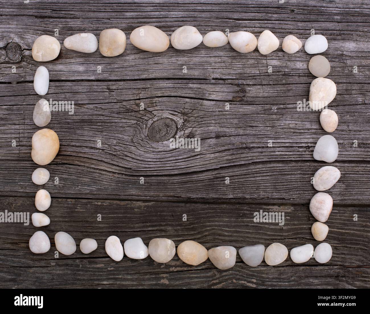 A rectangular frame of smooth white pebbles rests on a rustic weathered wooden surface. Stock Photo