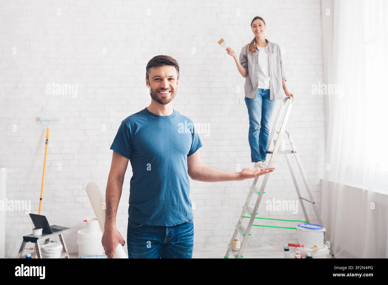 Man holding wife on palm while she painting walls Stock Photo
