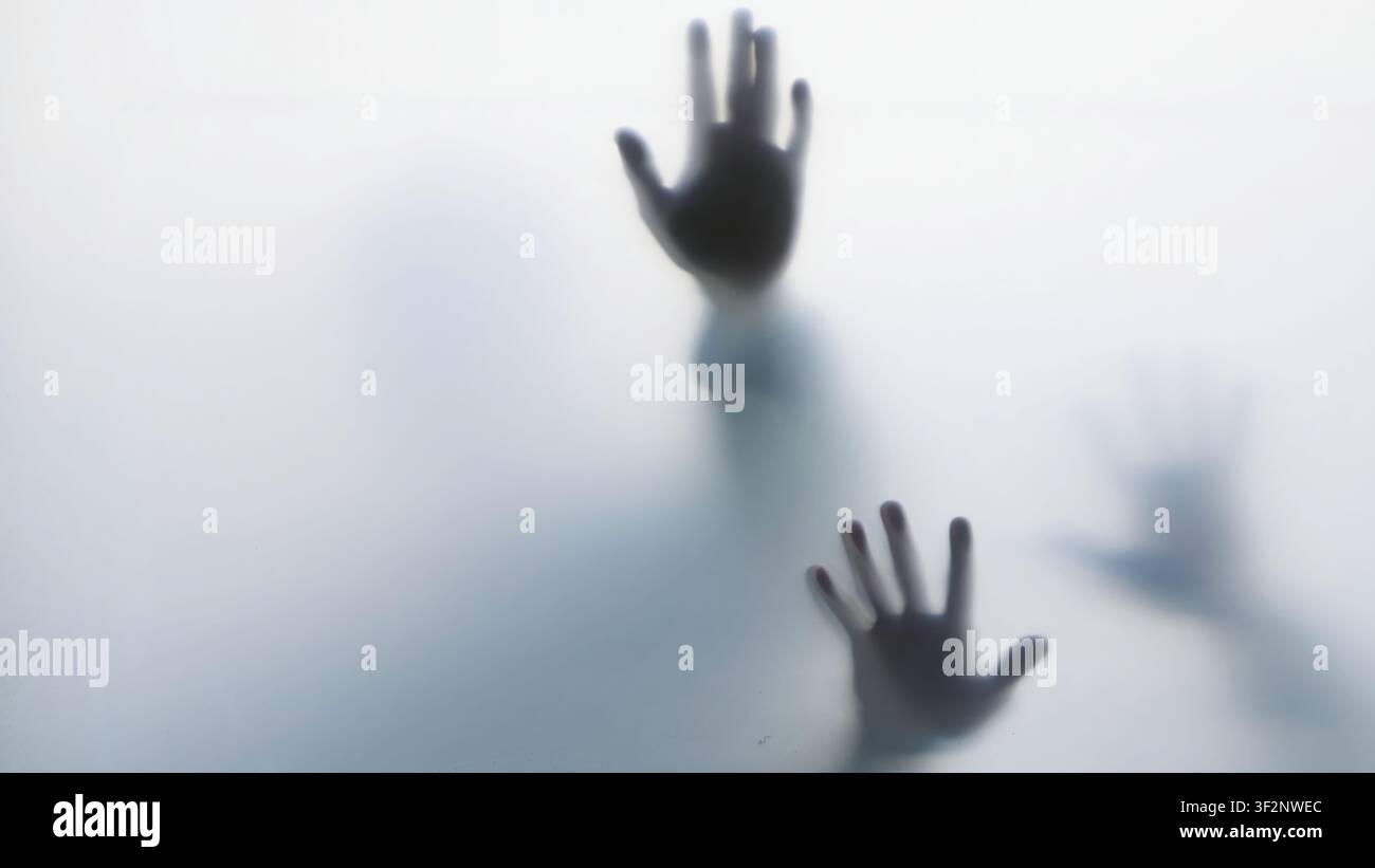 Dark hand silhouettes pressed against frosted glass Stock Photo
