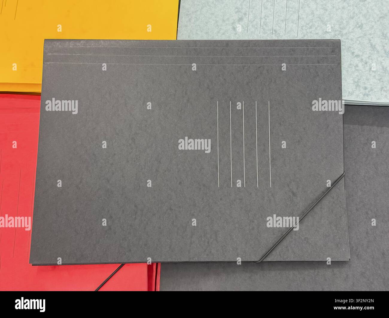 Black cardboard document folder with elastic closure placed on colorful office folders. Office stationery background for paperwork, organization Stock Photo