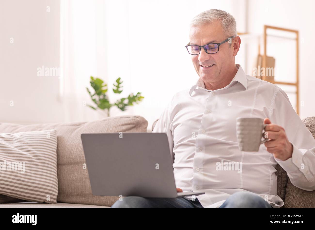 Elderly Man Using Laptop And Having Coffee Stock Photo