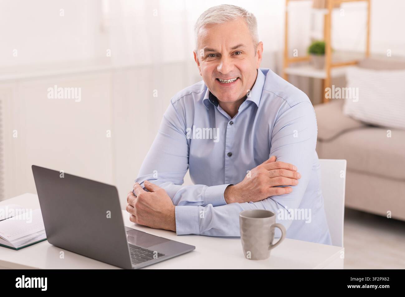Senior man using laptop at office and looking at camera Stock Photo