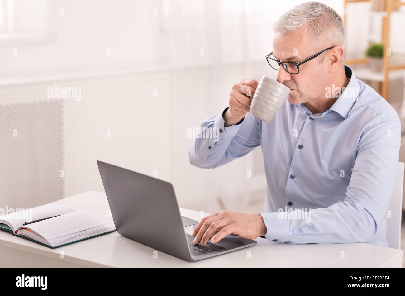 Happy senior man using laptop and drinking coffee Stock Photo