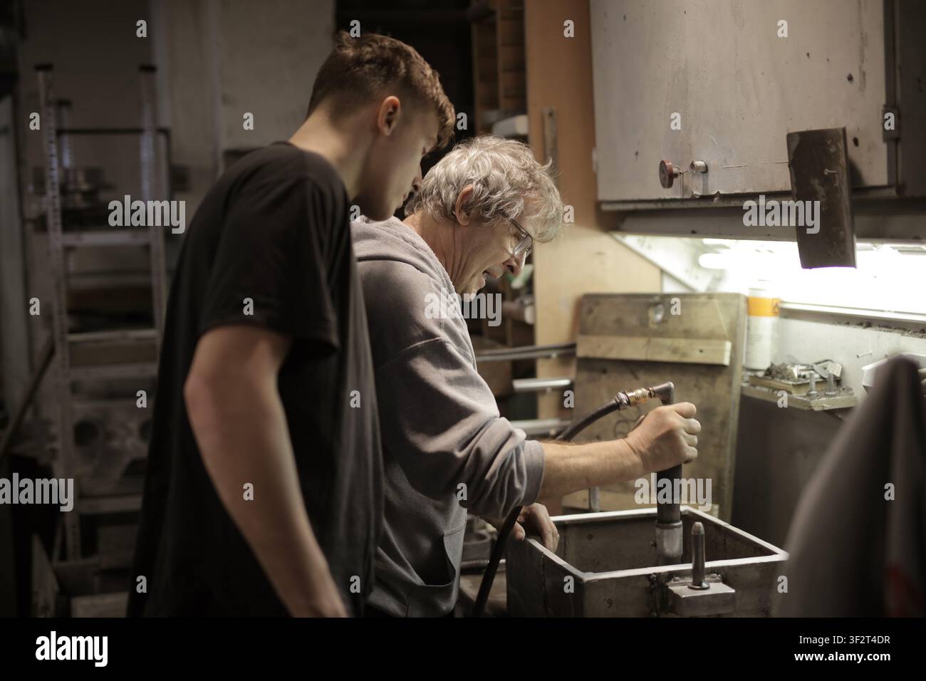 Older mentor teaches young apprentice in workshop Stock Photo