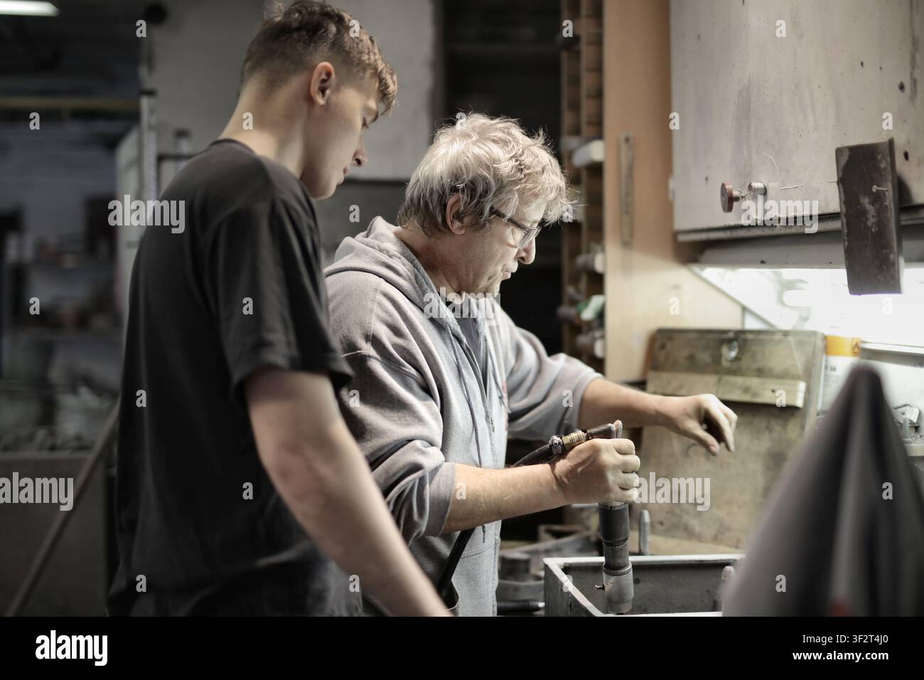 Senior craftsman teaches young apprentice in workshop Stock Photo