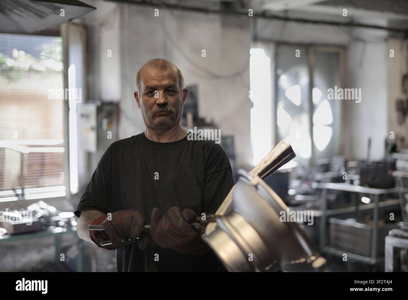Mature worker with mustache looks at camera in workshop Stock Photo
