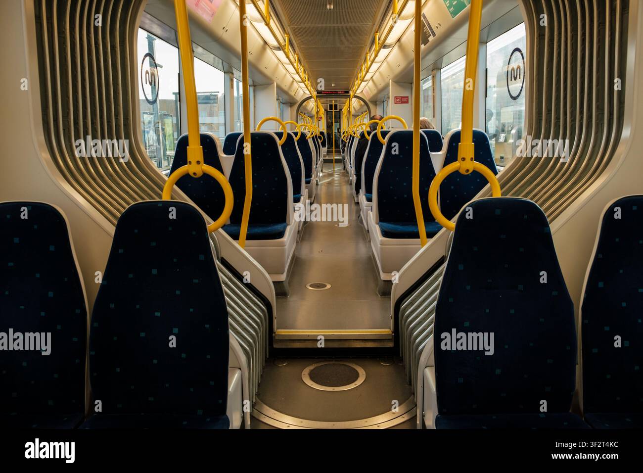 Clean train interior with rows of blue seats and yellow handrails, ready for public transportation Stock Photo