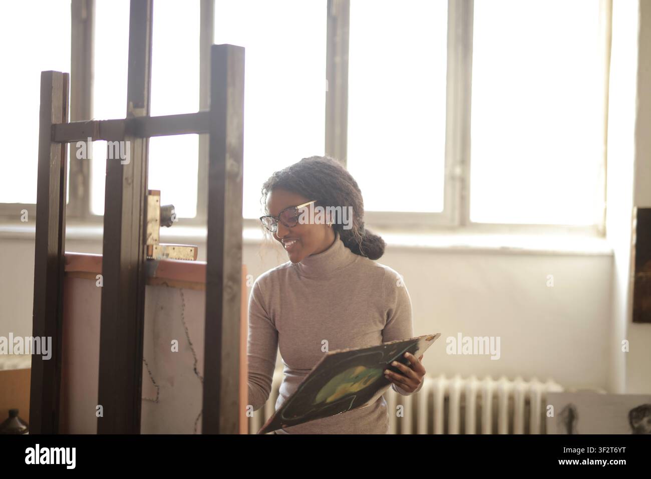 Smiling artist stands by easel in bright studio Stock Photo