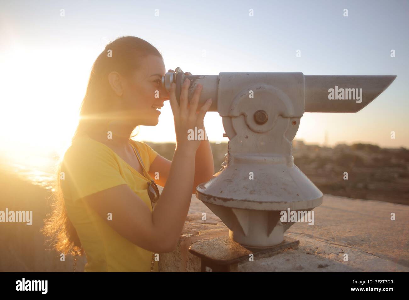 Smiling woman looking through scenic viewer at sunset Stock Photo