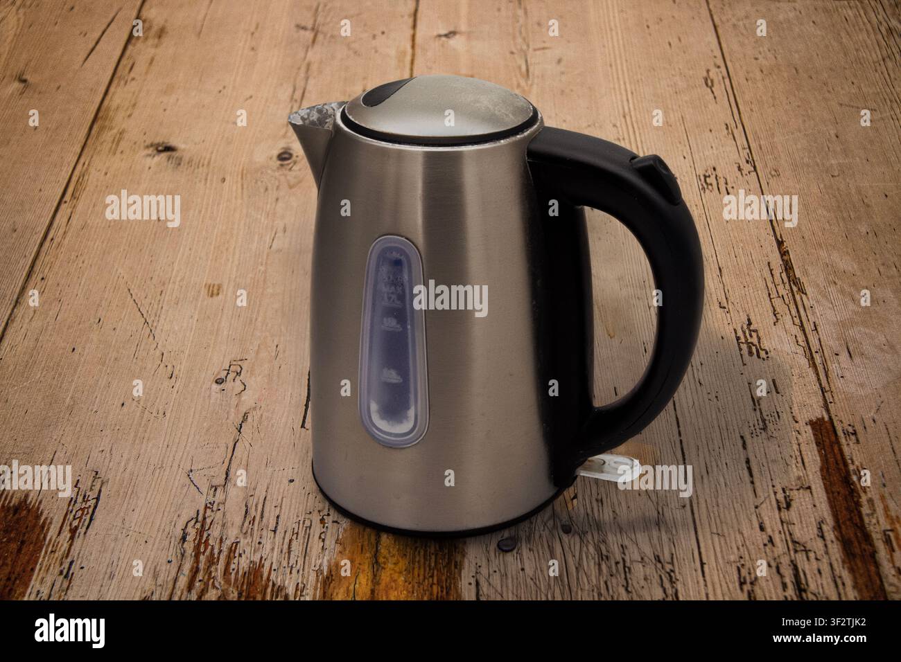 Used matt silver metal electric kettle for water heating with a large black plastic handle, water level indicator and on/off switch on a wooden table Stock Photo