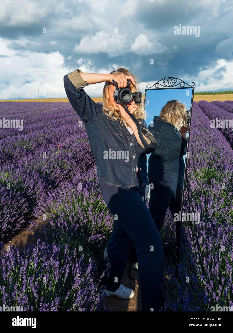 Portrait of Female Photographer Taking Photos in a Lavender Field Under Dramatic Blue Storm Sky.. Stock Photo