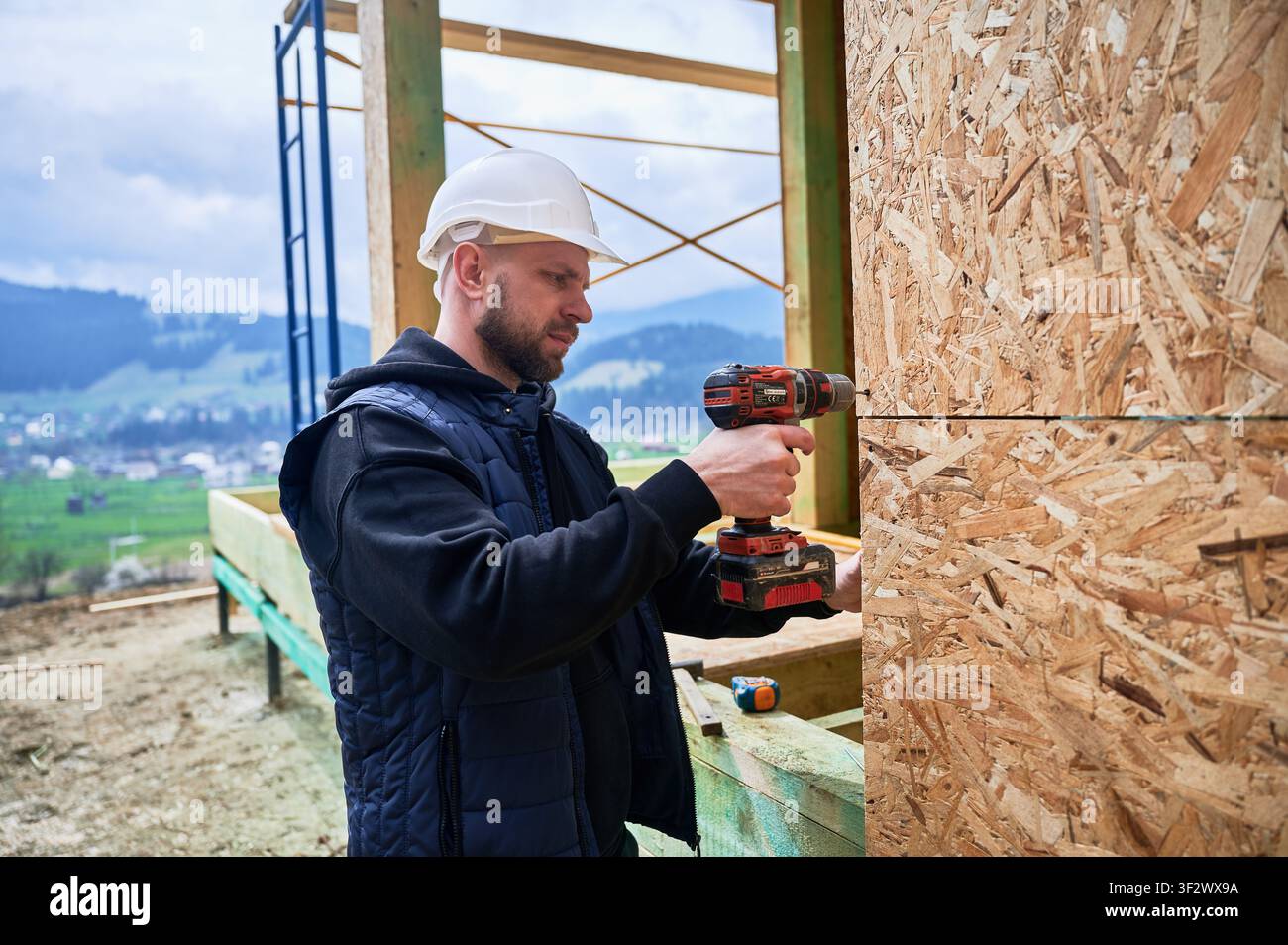 Construction worker installing OSB panels on wooden frame using cordless drill, representing wall assembly, home building process and structural development Stock Photo