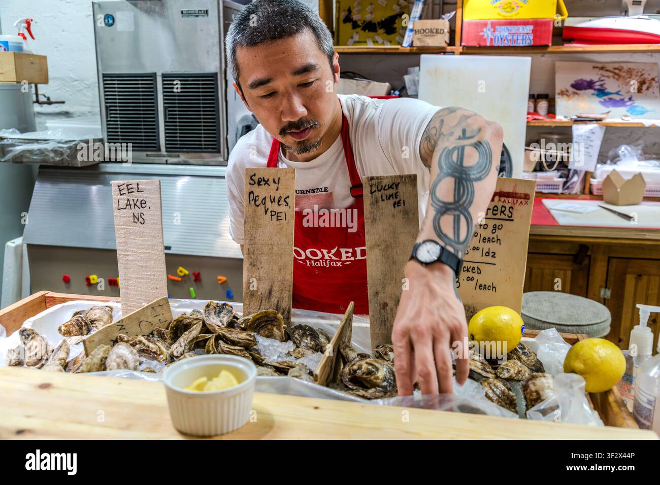 A sales assistant at the fishmonger’s Hooked Halifax sorts oysters from Eel Lake, Nova Scotia, and Prince Edward Island at his market stall in Keith’s Brewery Market on Lower Water Street in Halifax, Canada. Halifax, Nova Scotia, Canada Stock Photo
