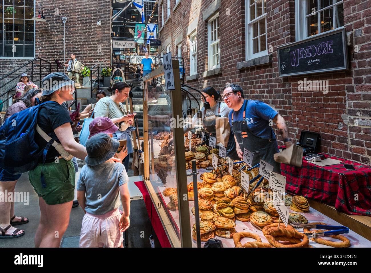 Staff at the vegan bakery The Mediocre Bakery serve customers at their stall in Keith’s Brewery Market on Lower Water Street in Halifax, Canada. Their range includes pretzels and puff pastries made from purely plant-based ingredients. Halifax, Nova Scotia, Canada Stock Photo