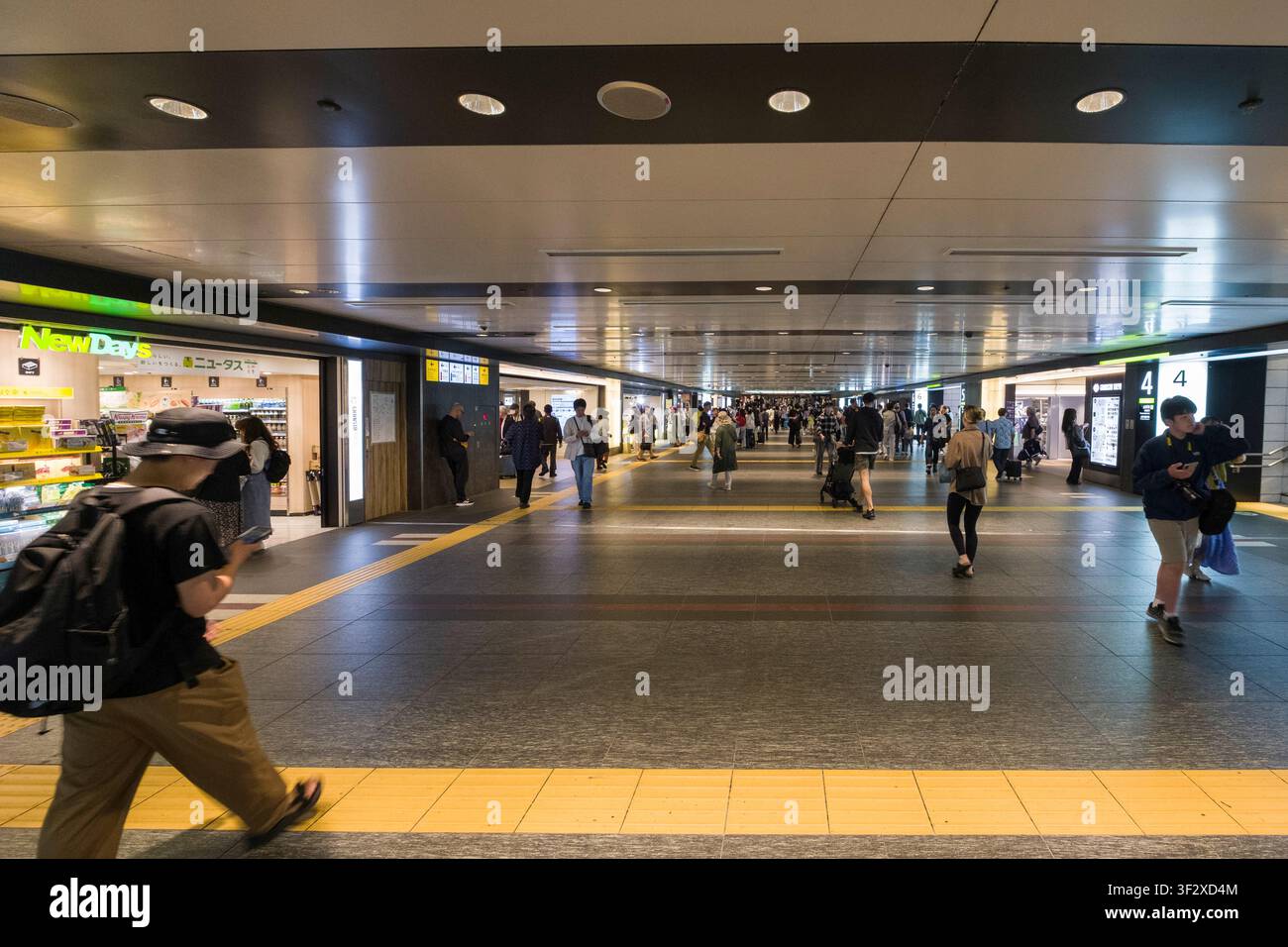 Tokyo Station's expansive interior bustles with activity as commuters and travelers navigate the lengthy passageways. Illuminated by modern lighting, Stock Photo