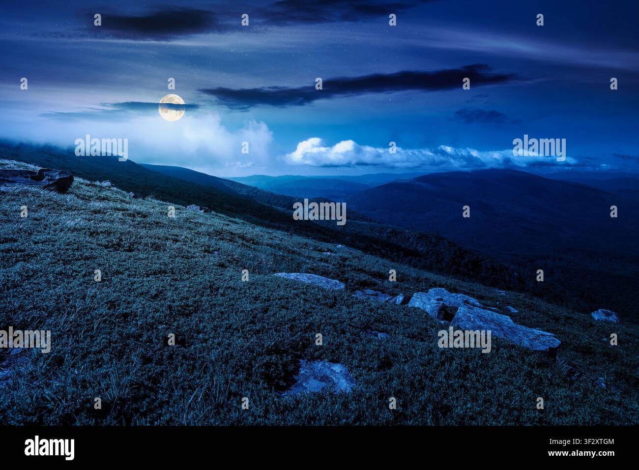 nature scenery with mountain under summer sky at night. full moon over alpine landscape of carpathian mountain with grassy slopes. low fluffy clouds o Stock Photo