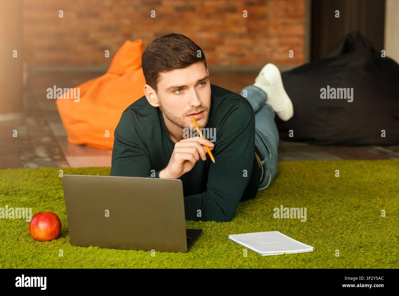 Guy Using Laptop Thinking Lying On Floor In Coworking Workspace Stock Photo