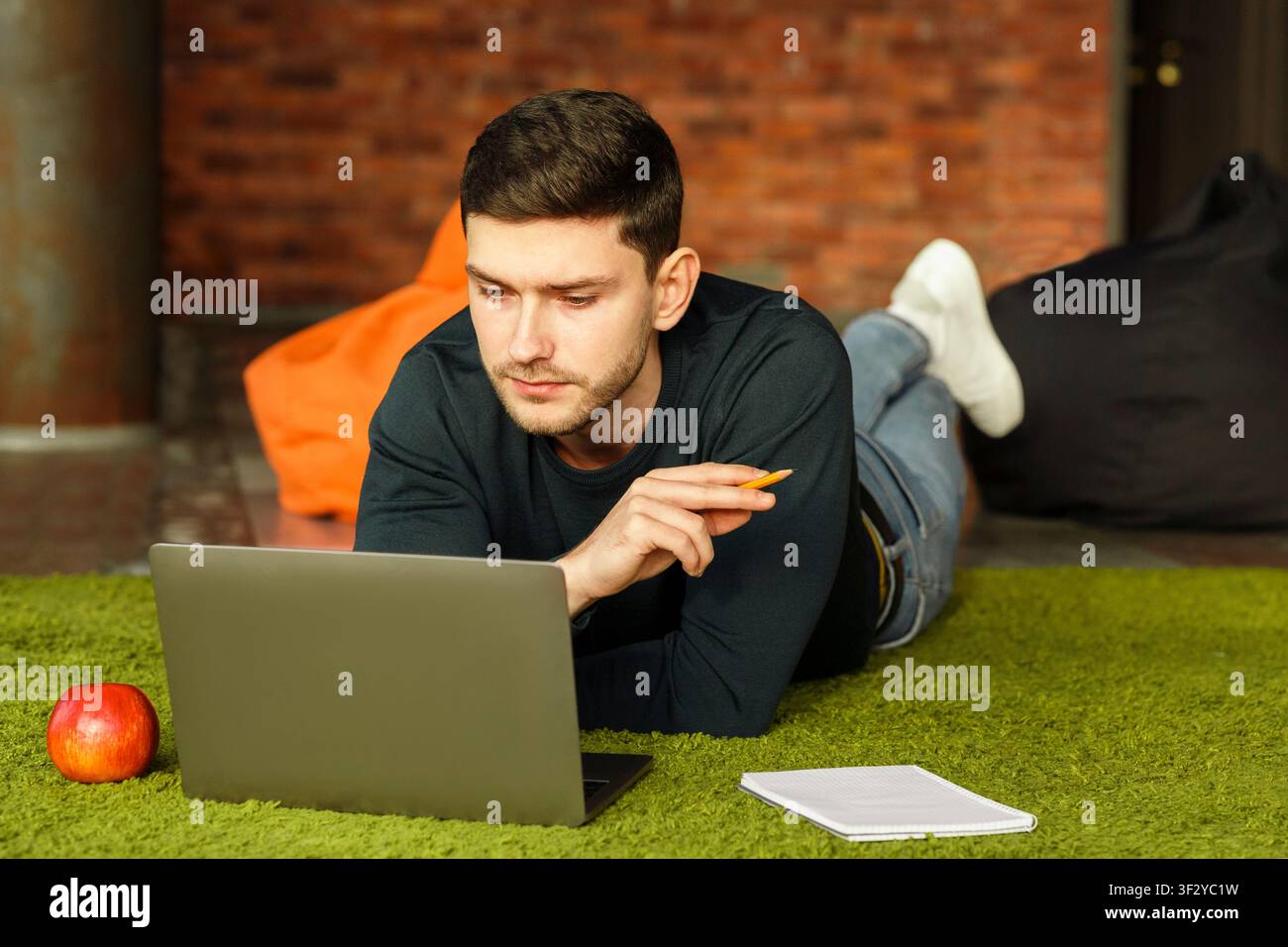 Millennial Guy Using Laptop Lying On Floor At Home Stock Photo