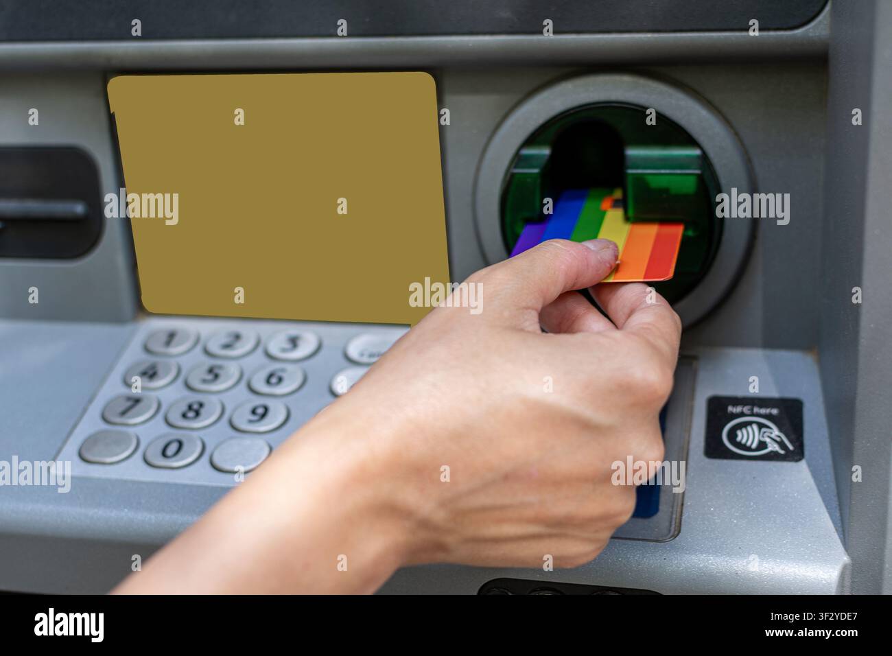 Hand inserting rainbow credit card into atm machine Stock Photo