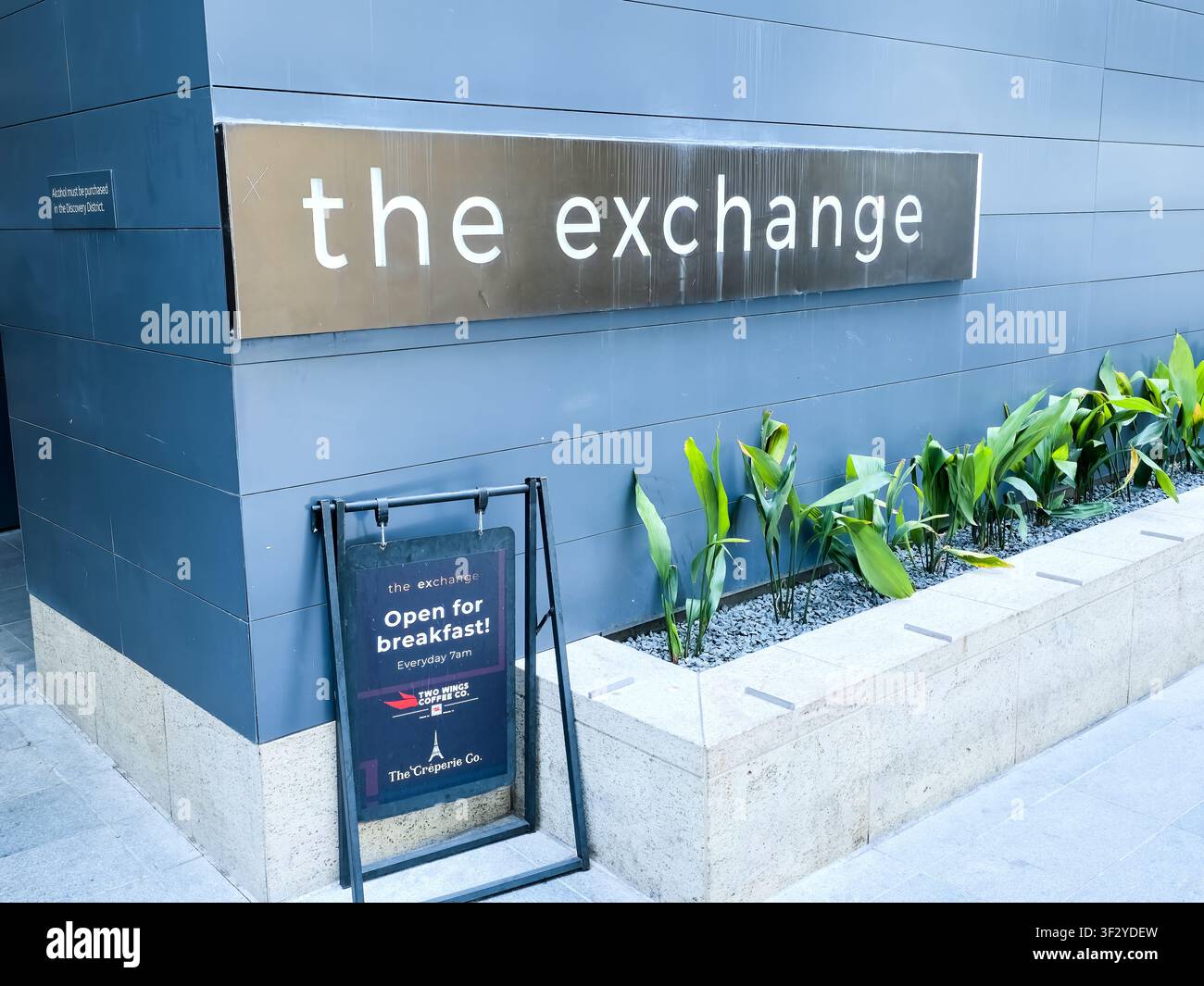 DALLAS, TX, USA - JULY 11, 2026: The entrance to The Exchange with a prominent sign visible against a modern building facade. Plants line the walkway, Stock Photo