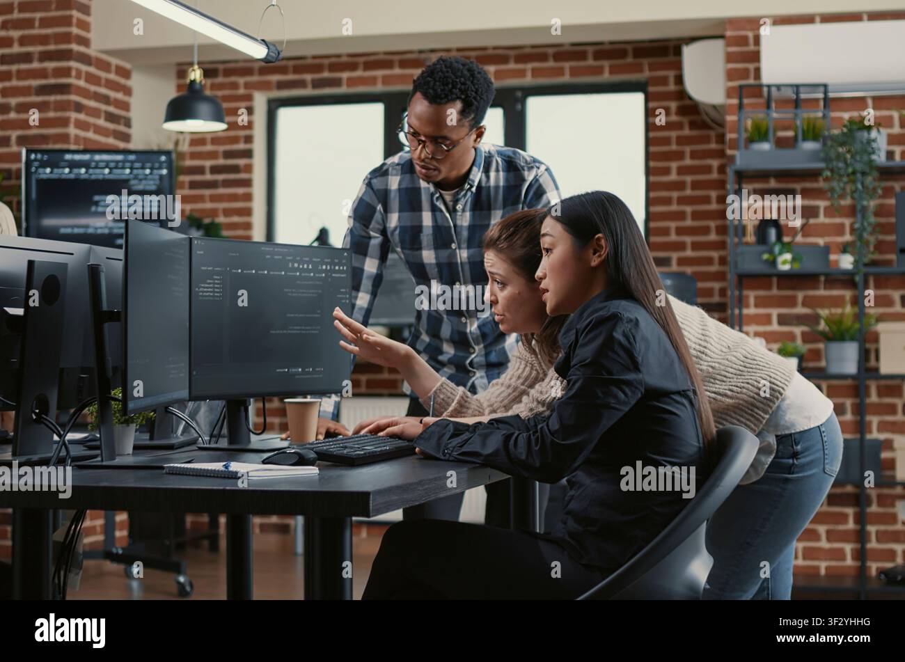 Mixed software engineers brainstorm cloud computing interface ideas while reviewing running code on computer screens in a development office. Stock Photo