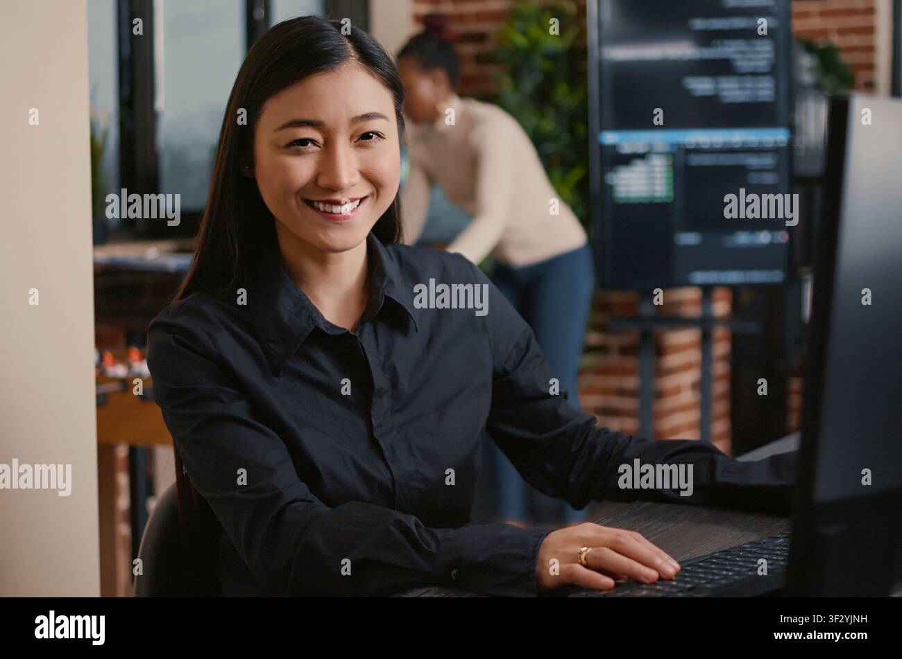 Asian software developer smiling and resuming work typing code on computer keyboard sitting at desk in big data office, with artificial intelligence and big data. Stock Photo