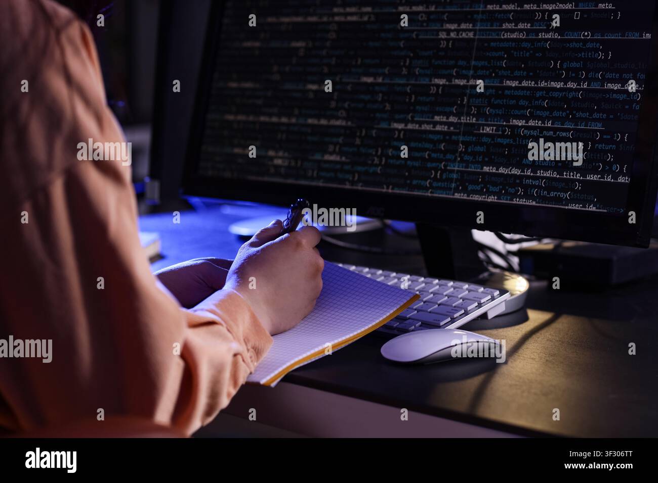 Female programmer working with notebook and computer in dark office at night, closeup Stock Photo