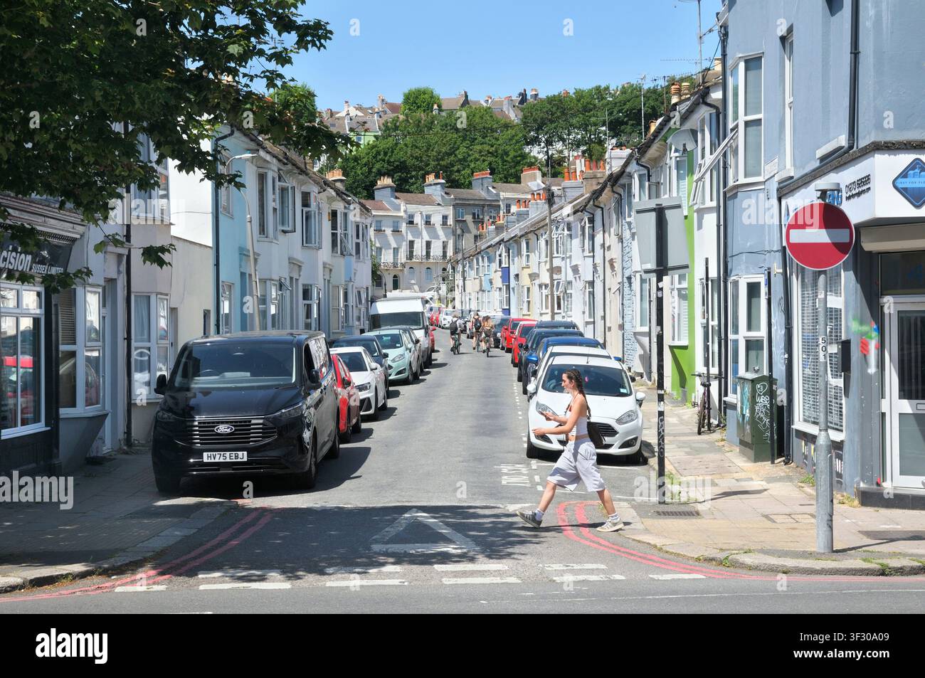 Young woman crossing St Paul's Street, a residential road with light pastel terraced houses in Round Hill area of Brighton, off Lewes Road, Sussex, UK Stock Photo