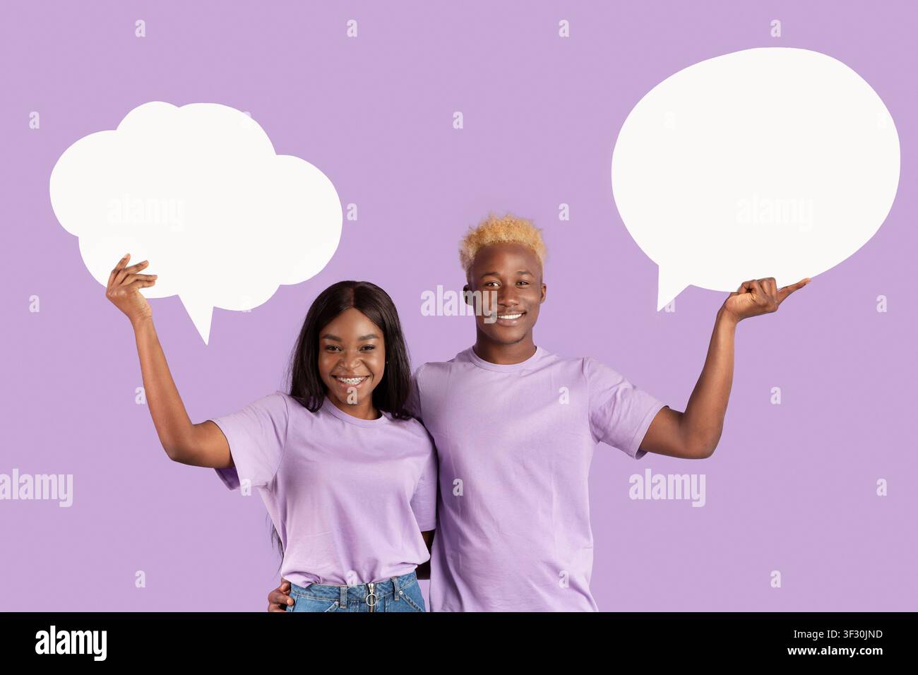 Millennial black couple holding empty speech bubbles on violet studio background, space for text Stock Photo