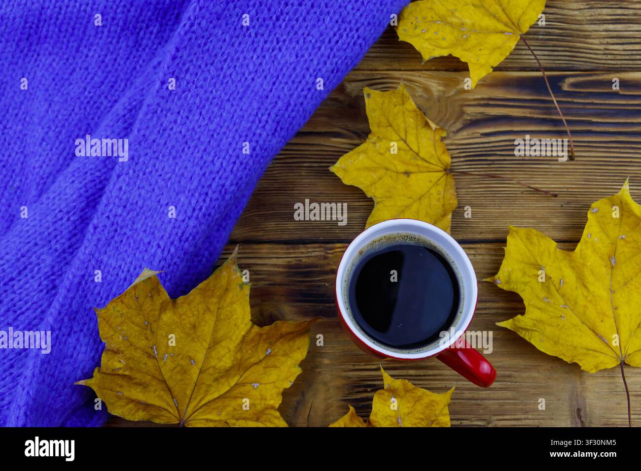 Cosy knitted blue sweater, cup of coffee and autumn maple leaves on wooden table. Top view. Autumn cozy concept Stock Photo