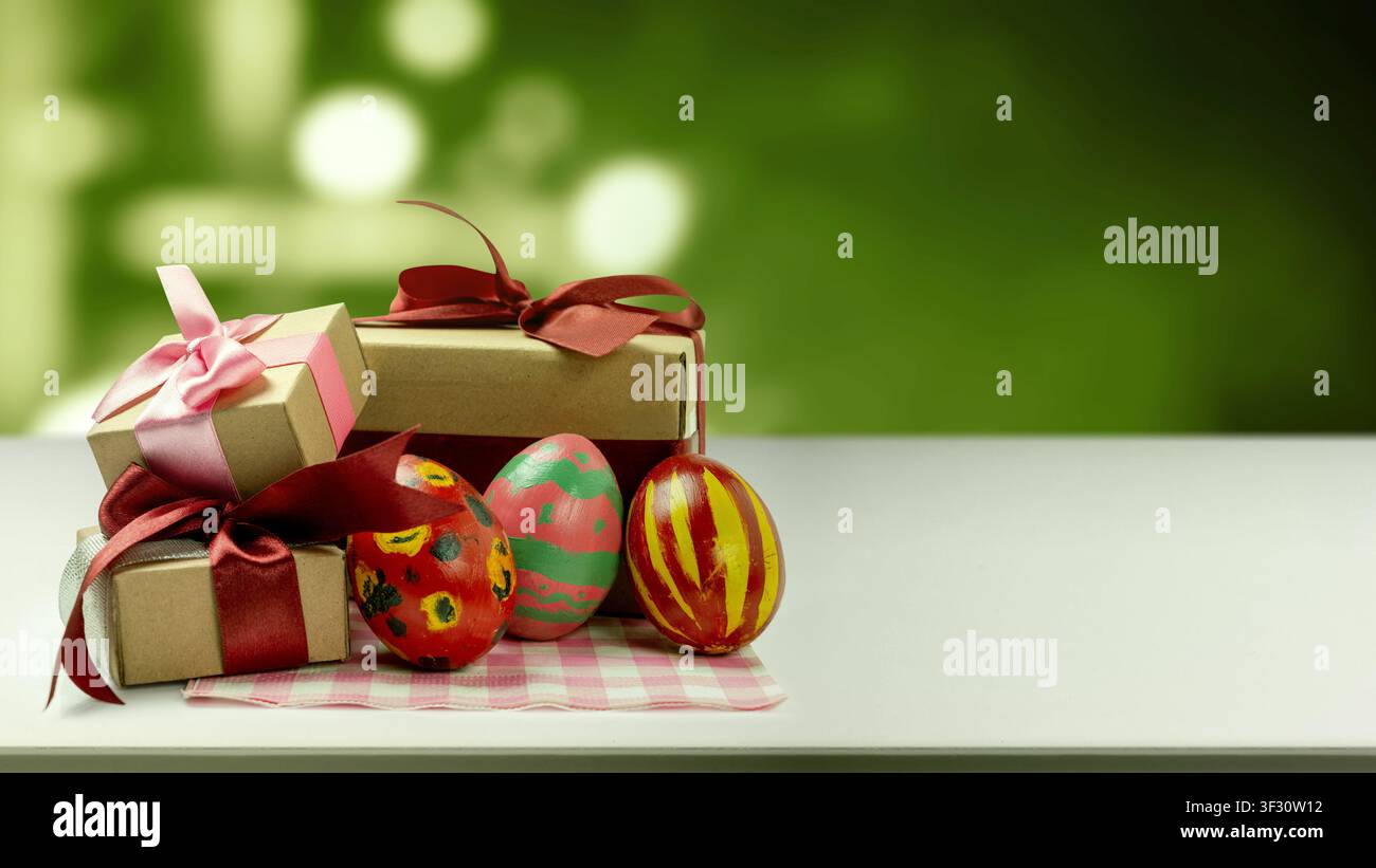 Painted Easter eggs with unique patterns and three brown gift boxes tied with pink and red ribbons on a white surface. Scene is set against a blurred Stock Photo
