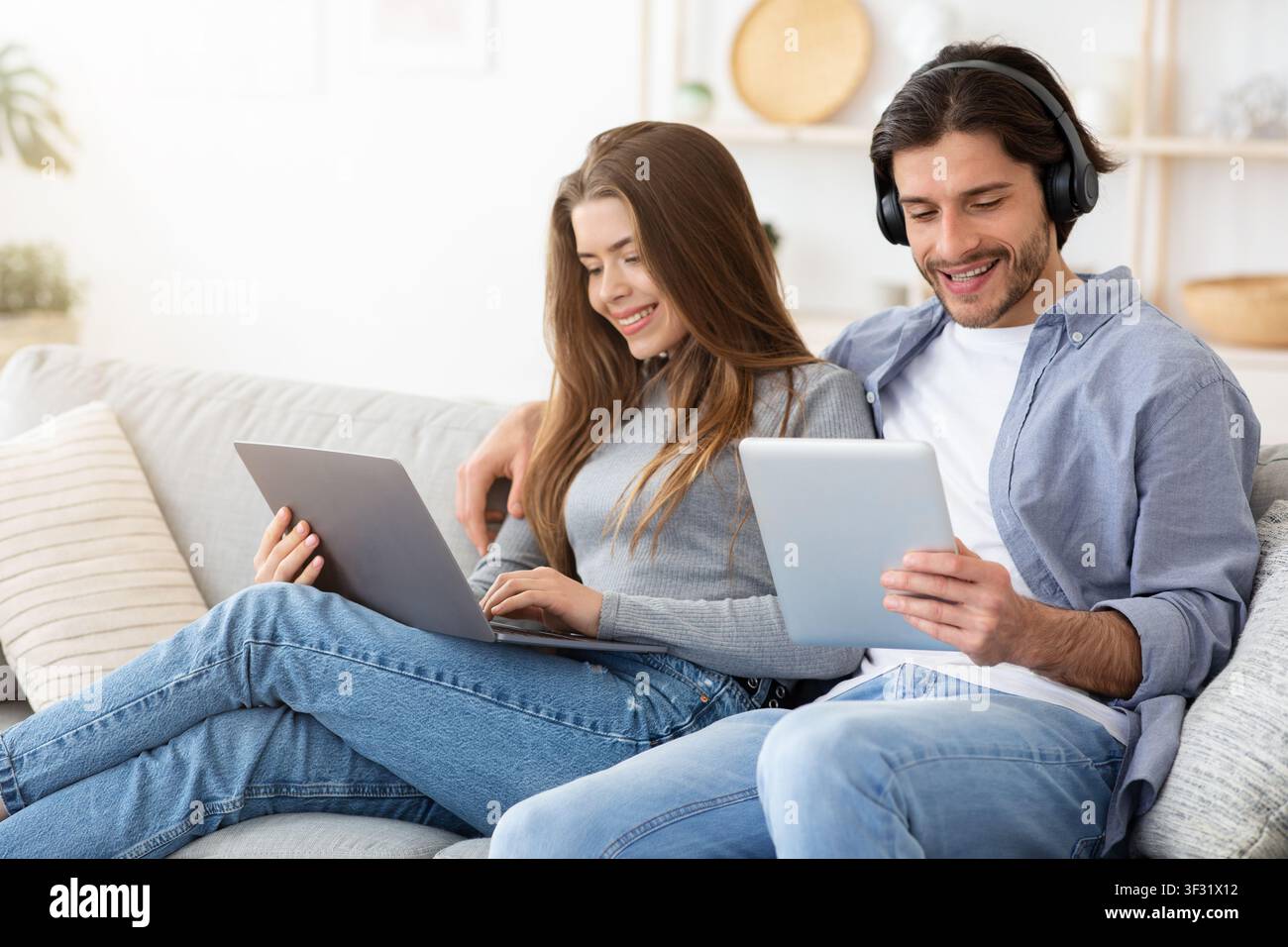 Smiling man and woman using electronic devices, home interior Stock Photo