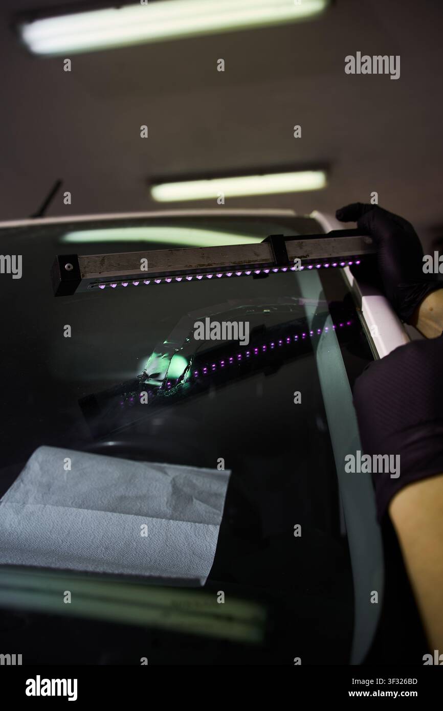 Mechanic cures resin inside windshield crack using lighting equipment. Windshield UV Resin Curing. Windshield repair. Automotive technician holds ultr Stock Photo