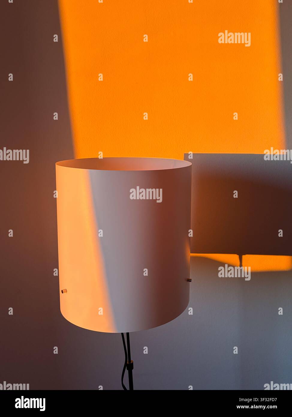 Minimal white floor lamp casting dramatic orange sunlight shadows on a white wall Stock Photo
