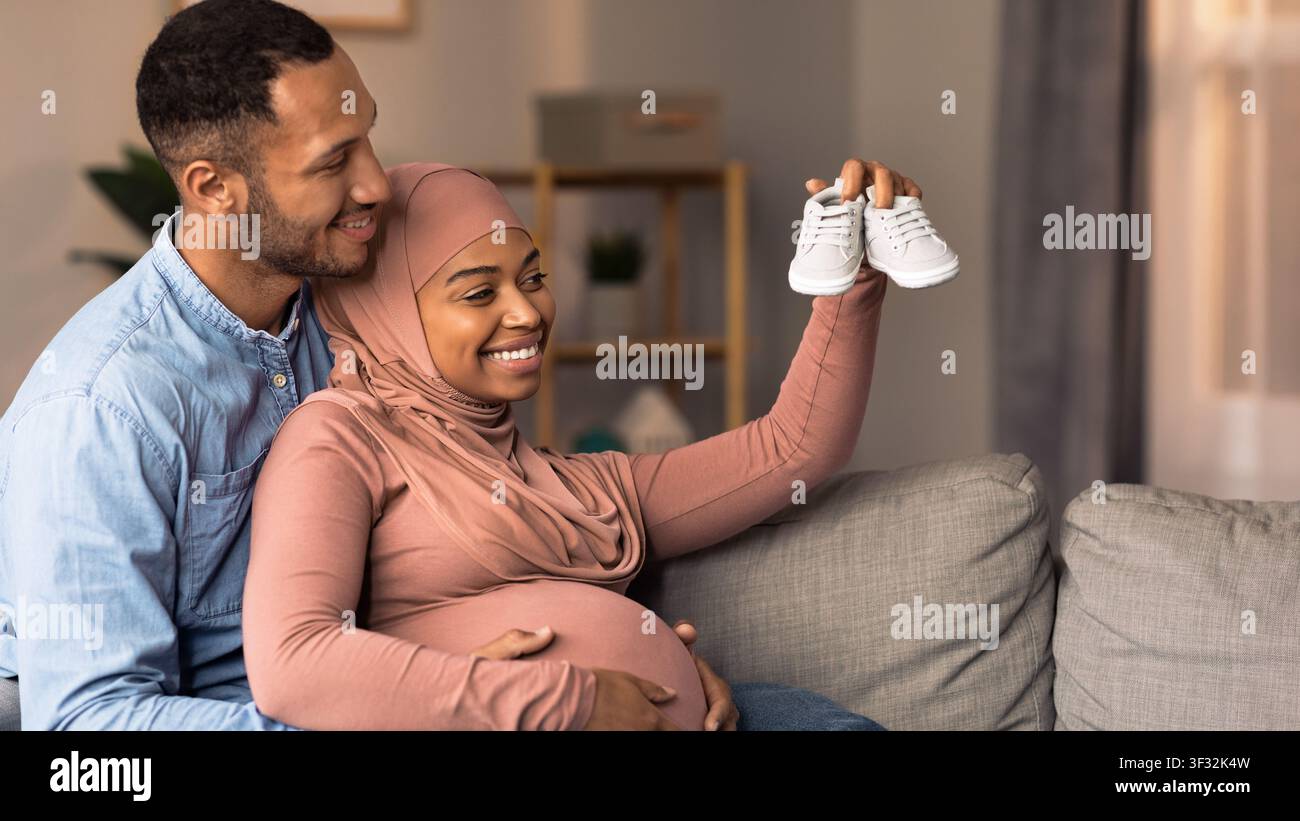 Happy African American Couple Expecting Baby, Holding Shoes Together At Home, Family Concept Stock Photo
