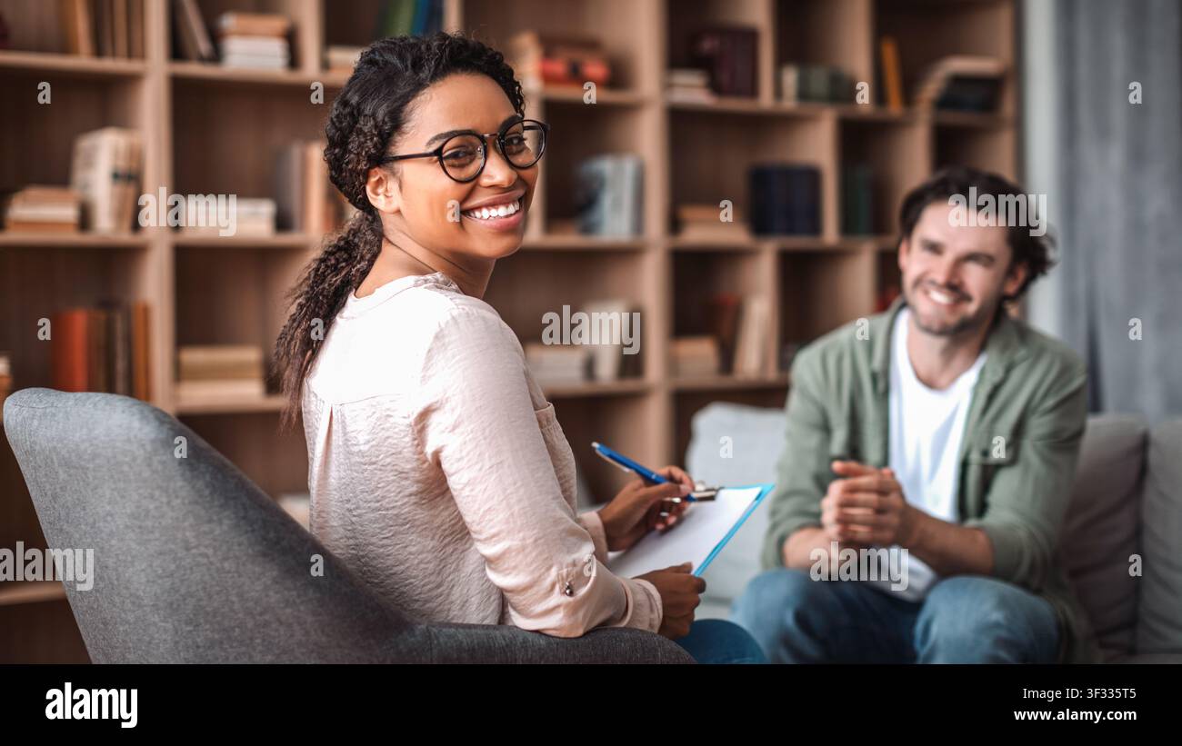 Smiling Young Black Woman Taking Notes During Counseling Session, Office Environment Stock Photo