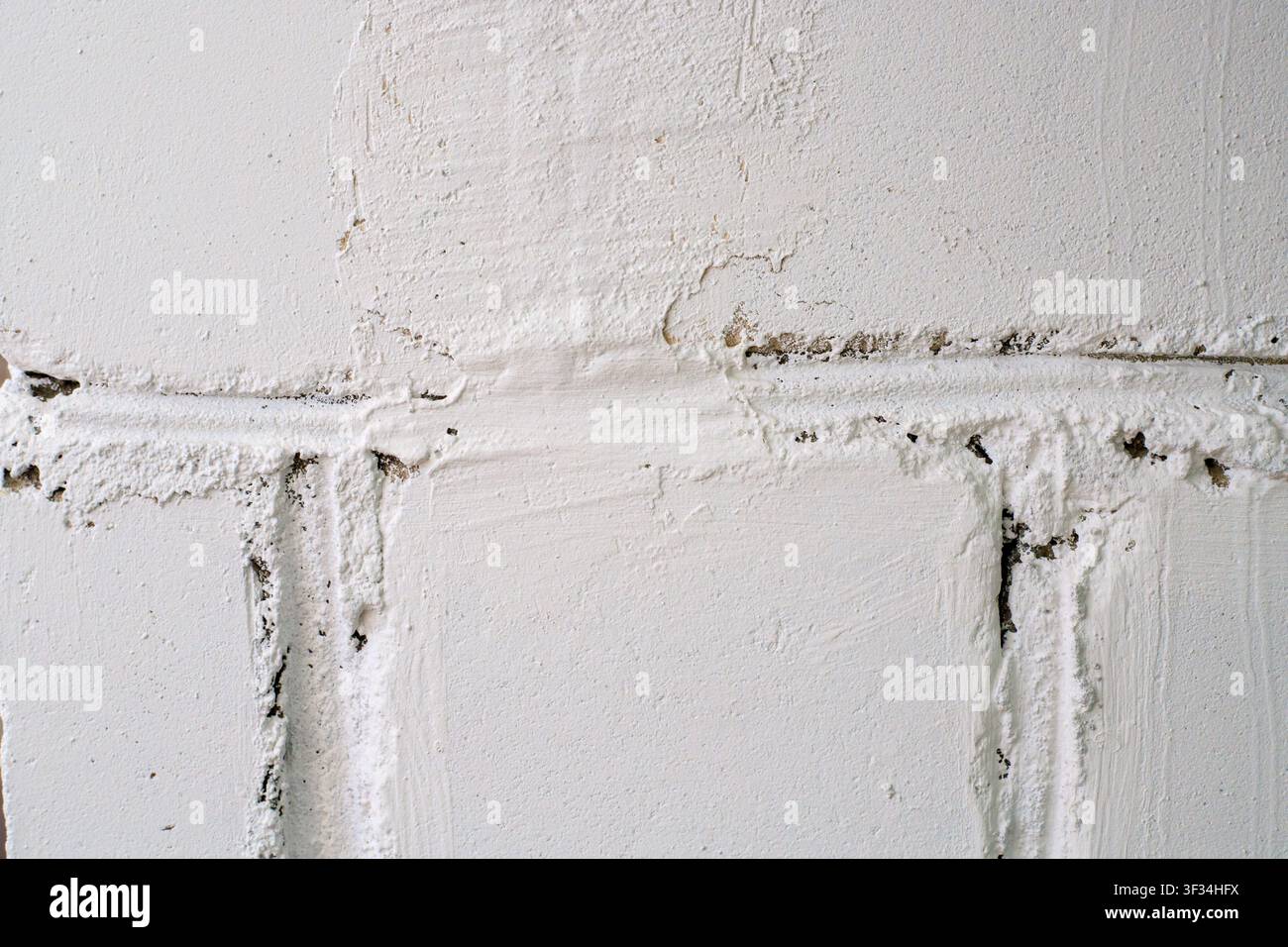 White painted block wall texture. White concrete bricks with messy mortar layers, uneven surface, and cracks in building construction Stock Photo