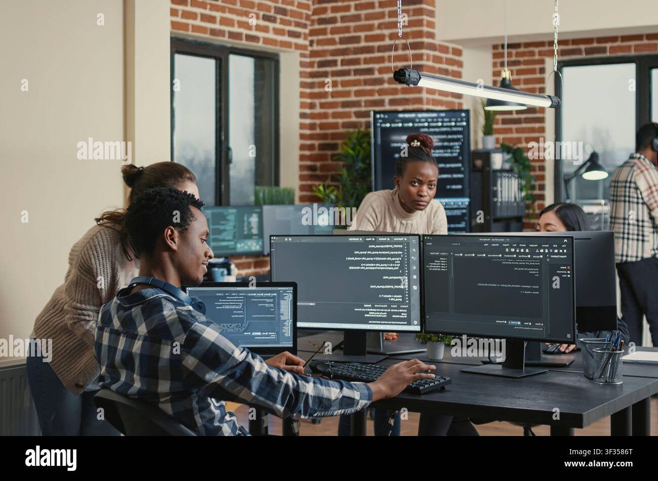 Programmer analyzing compiling code on multiple screens takes off glasses and doing high five hand gesture with colleague developer, software developers celebrating successful coding. Stock Photo